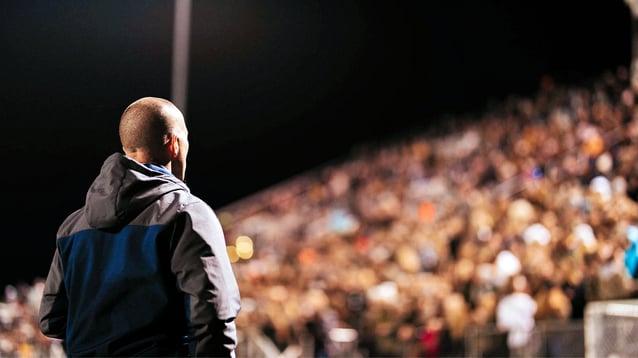 Athletic Director standing on the field looking up at the stands packed with fans on a game night.