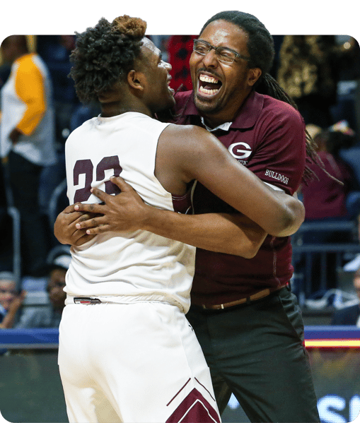 Basketball coach and player celebrating together on the court and hugging.